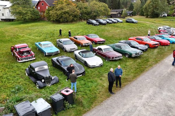Aerial view of a vintage car show on a grassy field with rows of classic cars and people strolling among them.